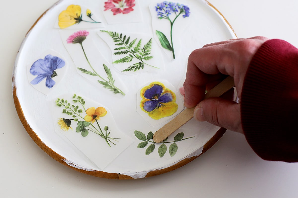 Applying rub-on transfers to a wooden platter with a wooden stick.