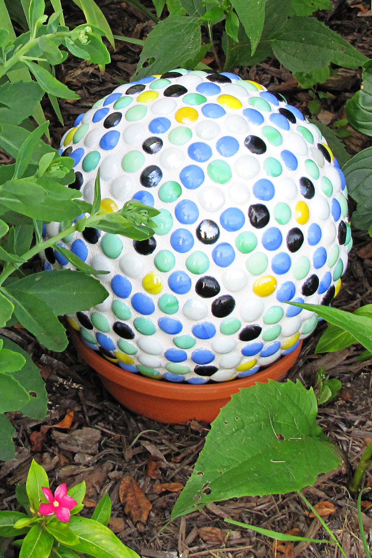 Bowling ball yard art made from covering a bowling ball with mosaic gems and displaying in the garden.