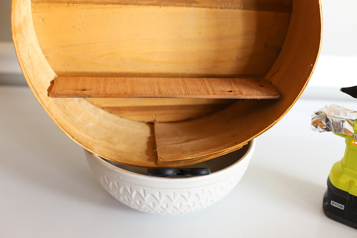 The small wooden shelf glued to the bottom of the round vintage wooden cheese box. 