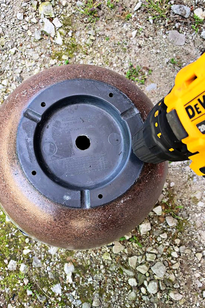 Drilling holes in the bottom of a flower pot being used as a garden hose holder.