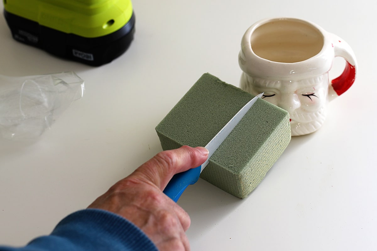Cutting floral foam to fill in the Santa mug so it can hold Christmas decor.