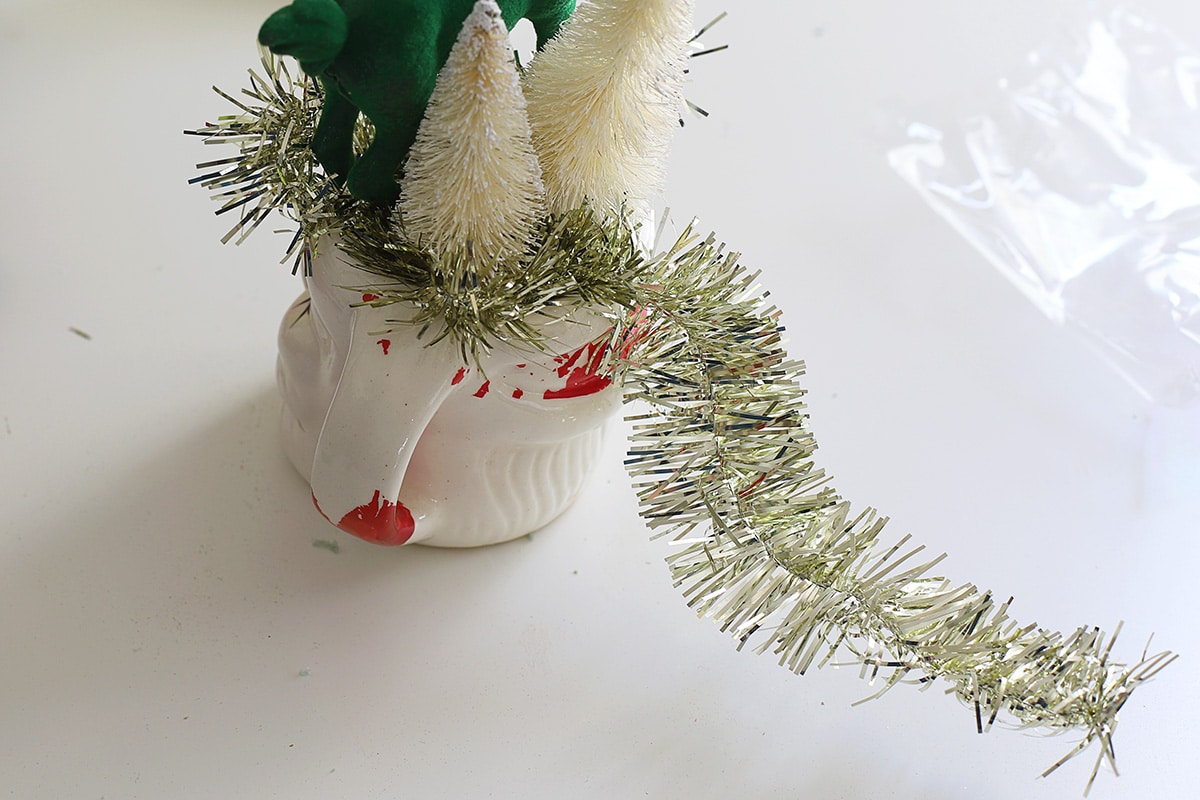 Tinsel garland streaming out the top of a vintage Santa mug.