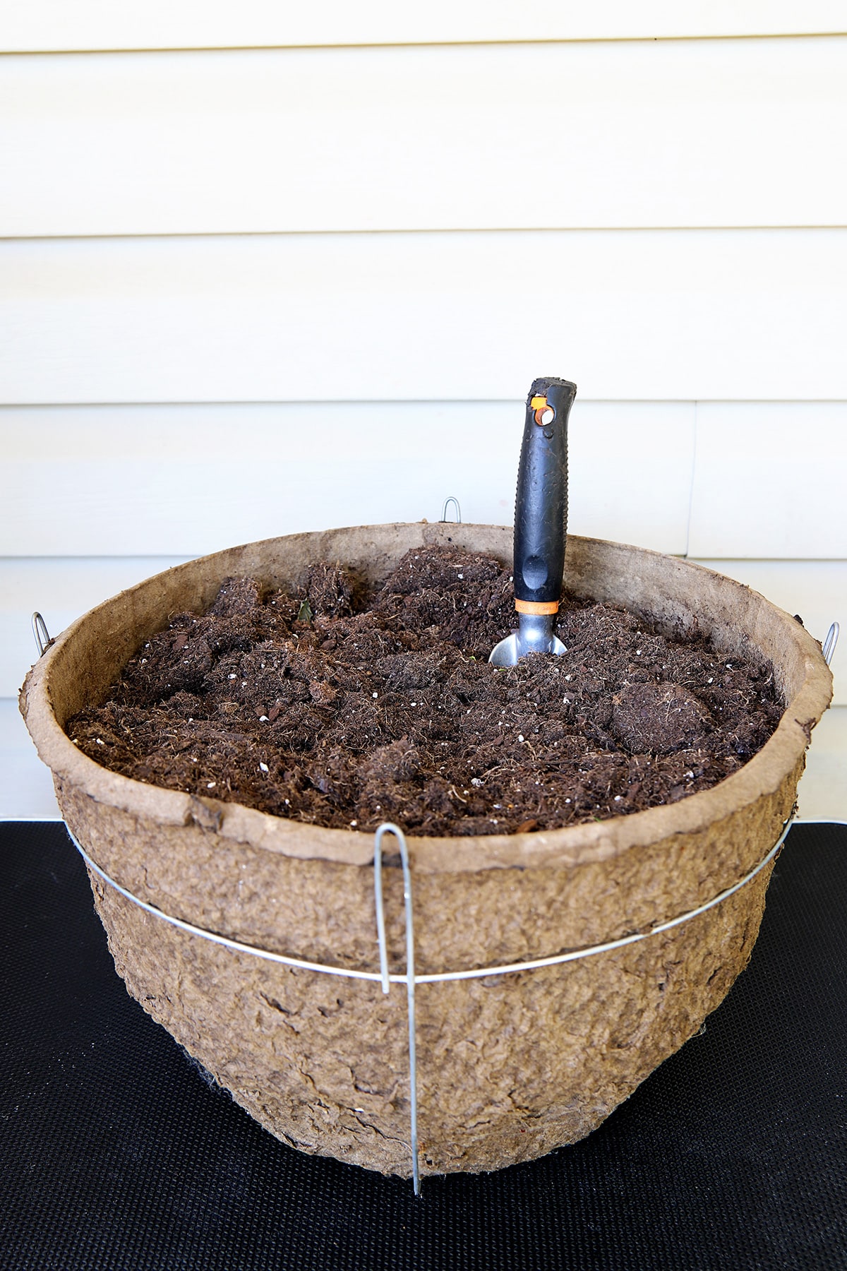 a planting container full of potting soil with a hand trowel sticking out of it. My dog has eaten the handle of the hand trowel becuase she loves to steal my hand tools when I'm not looking. 