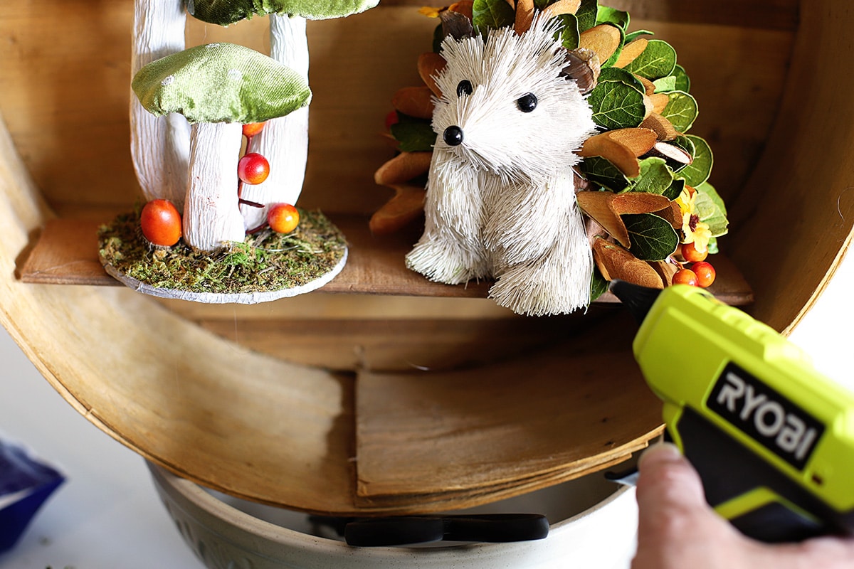 Using the hot glue gun to attach the sisal woodland creatures to the shelf in the cheese box. 