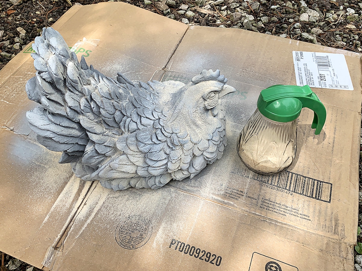 Shaking sand onto the first coat of spray paint in order to create a faux concrete look.