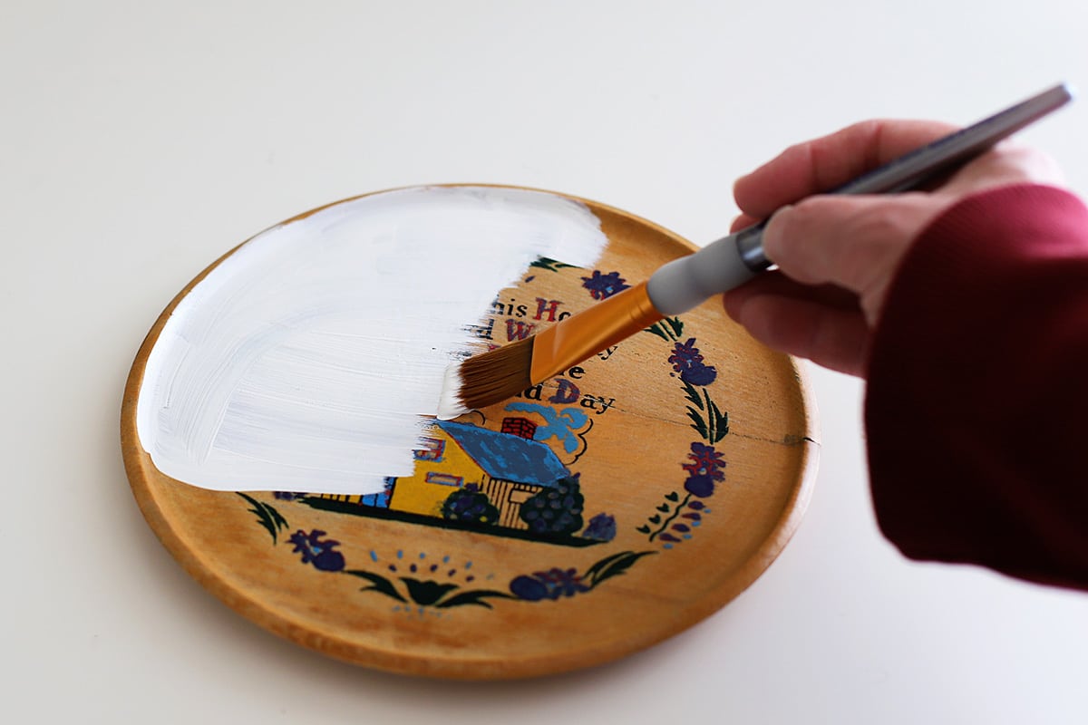 Painting a wooden plaque with white paint.
