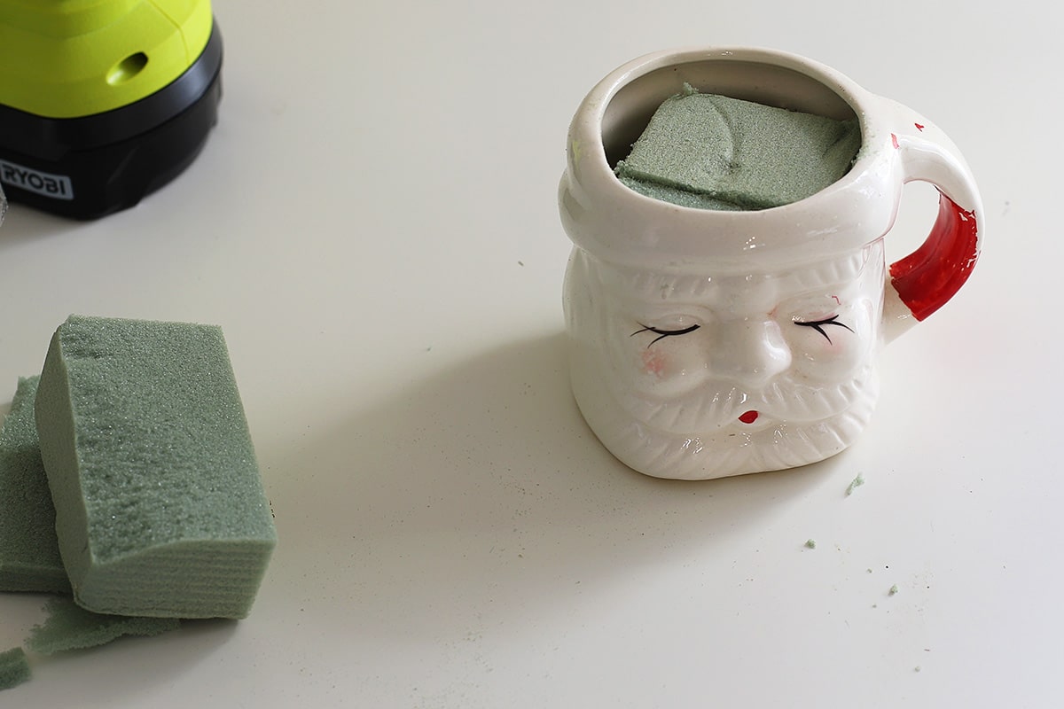 Santa mug with styrofoam placed inside it to hold Christmas ornaments.