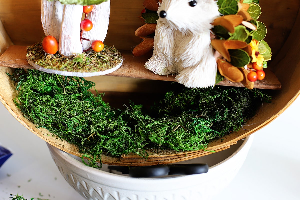 Gluing the green moss to the inside bottom of the cheese box to create a woodland forest floor for the fall wreath.