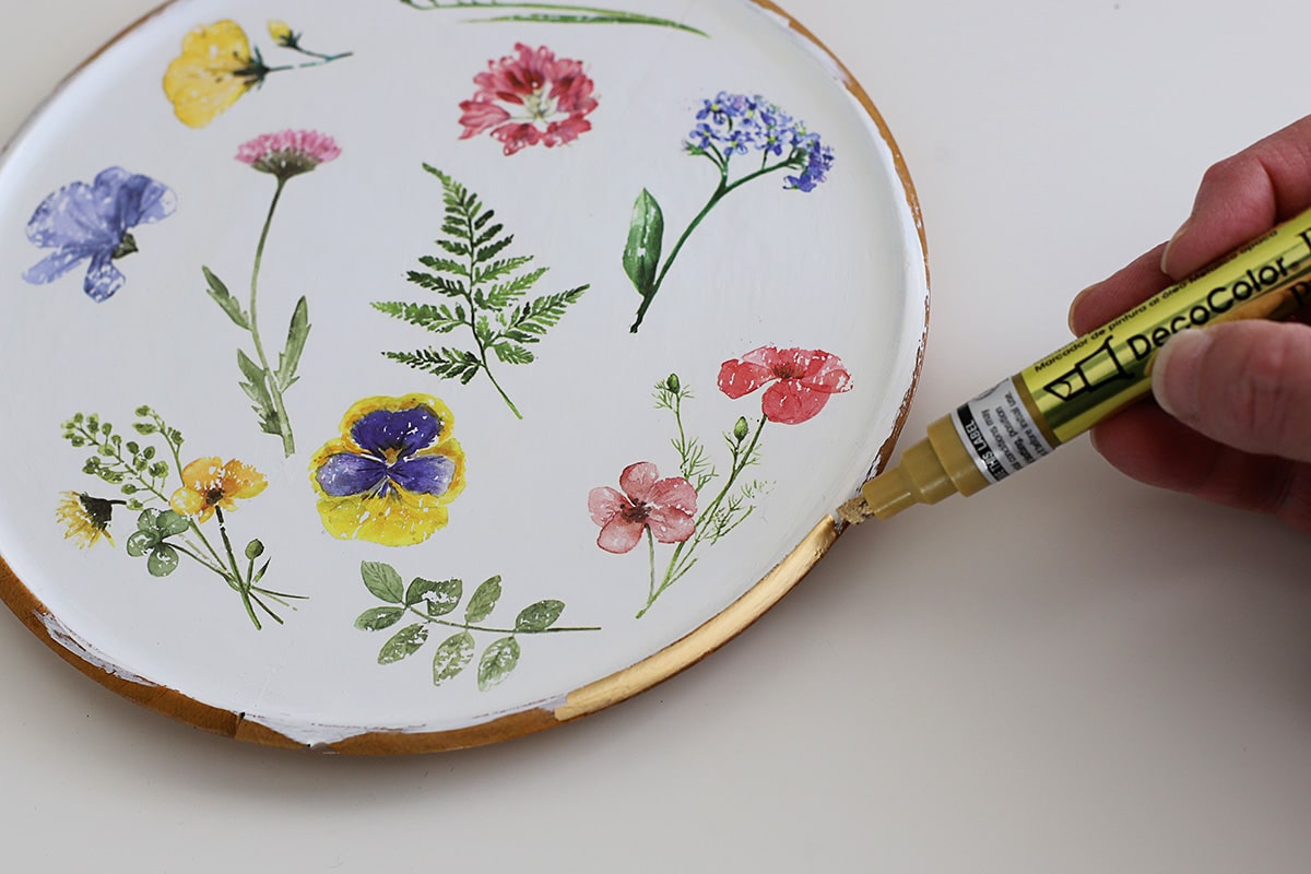 Using a paint marker to apply gold leaf to the perimeter of a wooden platter.